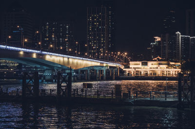 Bridge over river against illuminated buildings in city at night