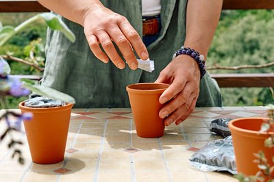 Woman sowing medicinal or aromatic herbs in clay pot on balcony. home planting and food growing.