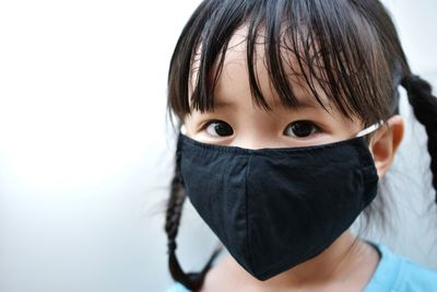 Close-up portrait of girl wearing mask against white background