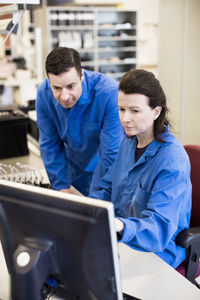 Male and female technicians using computer together at desk in industry