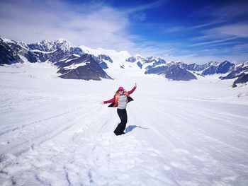 Happy woman with arms outstretched enjoying on snow covered field against mountains