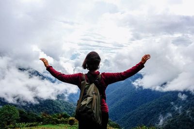 Rear view of woman with arms outstretched standing against cloudy sky