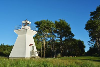 Lighthouse by trees on field against clear sky