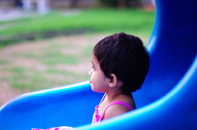Side view of girl sitting on blue slide at playground