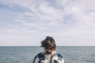 The man's face covered by hair against the backdrop of the sea in winter.