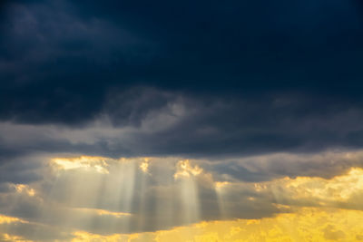 Low angle view of sunlight streaming through clouds