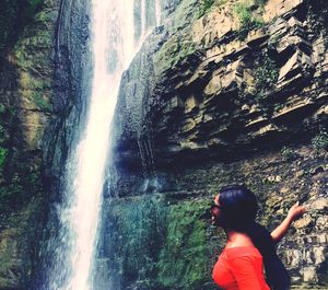 Rear view of woman standing on cliff against waterfall