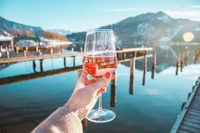 Female hand with glass of rose wine. cozy pier on the coast of lake tegernsee. mountains in bavaria
