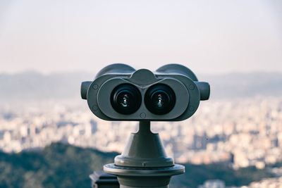 Close-up of telescope against sky and city view