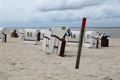 Hooded chairs on beach against sky