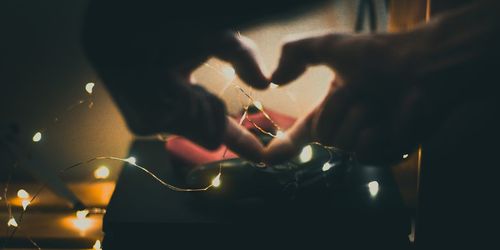 Midsection of person making heart shape with illuminated lights