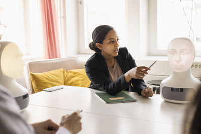 Businesswoman presenting robot voice assistant during meeting