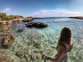 Rear view of woman on rocks at beach against sky