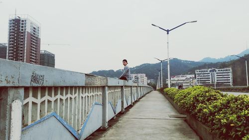 Man sitting on bridge by road in city