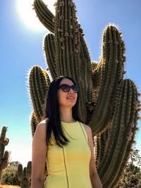 Portrait of smiling young woman wearing sunglasses against tall cactus and sky.