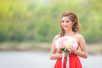 Portrait of a smiling young woman standing against plants