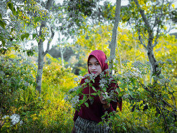 Portrait of young woman standing by plants