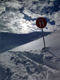 Road sign on snow covered landscape against sky