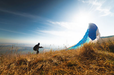 Paragliders take off from a yellow meadow, a man's legs open from the ground, taking off with a