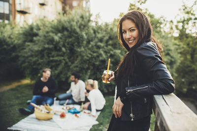 Side view portrait of happy woman holding elderflower drink during rooftop party with friends