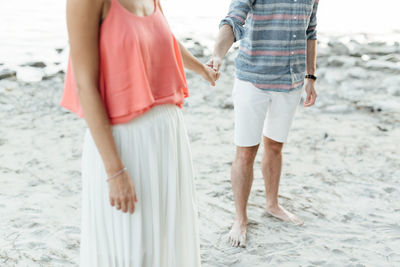 Low section of couple with holding hands standing at beach