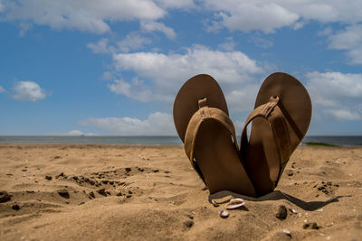 Low angle view of shoes on beach against sky