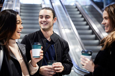 Cheerful friends talking while having coffee against escalators