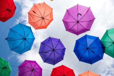 Directly below shot of multi colored umbrellas hanging against cloudy sky
