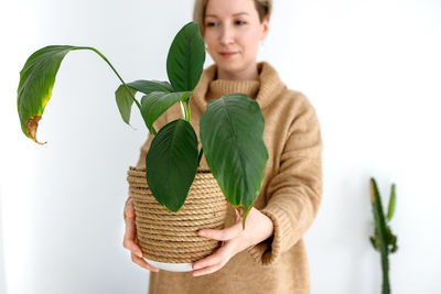 Portrait of woman holding plant against wall