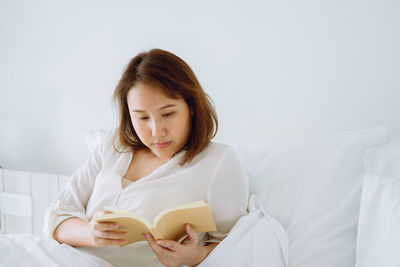 Woman reading book while sitting on bed at home