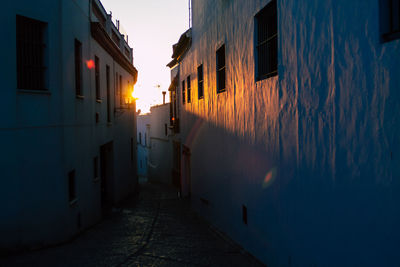 Narrow alley amidst buildings in city at sunset