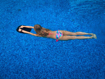 Young woman with colorful swimming suit swimming in the pool using a swimming kickboard