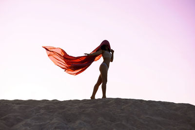 Rear view of woman standing on rock against clear sky