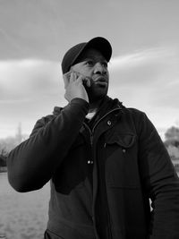 Man talking over phone while standing against sky