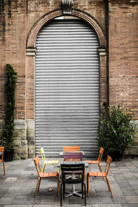 Chairs and tables on sidewalk against corrugated iron