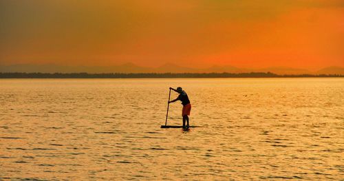 Side view of man paddleboarding on sea during sunset