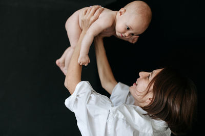 Side view of woman holding her baby against black background