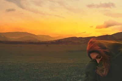 Woman relaxing on field against sky during sunset