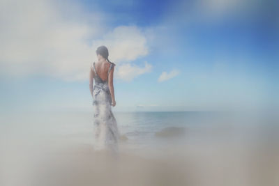 Rear view of man standing in sea against sky