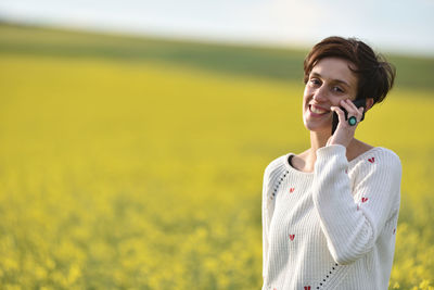 Young woman smiling while standing on field against sky