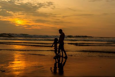 Silhouette men on beach against sky during sunset