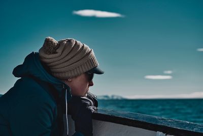 Side view of woman wearing hat on railing of boat on sea against blue sky