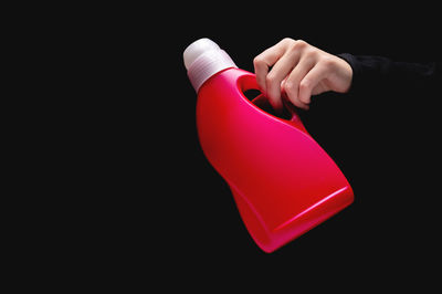 Cropped hand of woman holding yellow container against black background