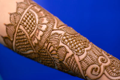 Close-up of woman hand with henna tattoo against blue background