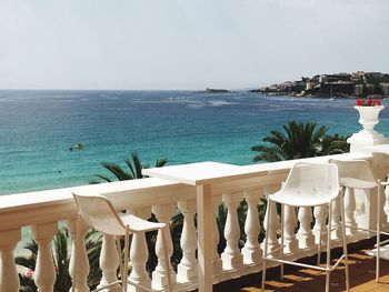 Chairs and table by sea against clear sky