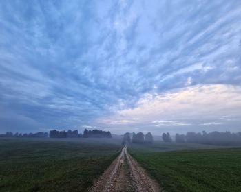 Empty road amidst field against sky