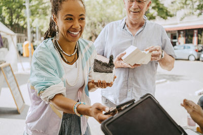 Smiling female customer holding house model while doing mobile payment at flea market