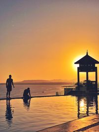 Silhouette people in swimming pool against sea during sunset