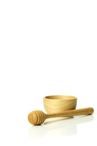 Close-up of wooden bowl with honey dipper against white background