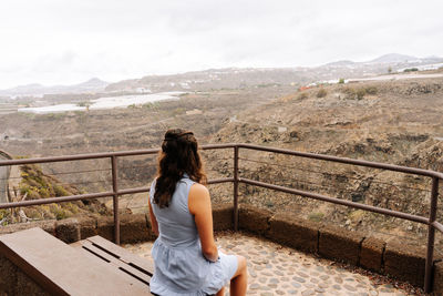 Rear view of woman sitting on railing against mountain